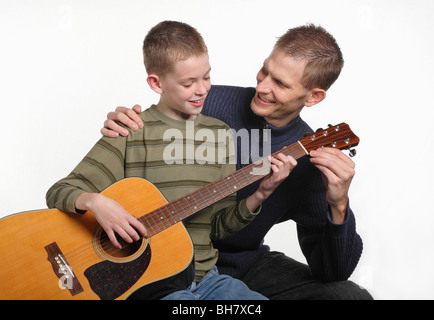 mid-adult father smiling and teaching elemetary age son how to play guitar Stock Photo