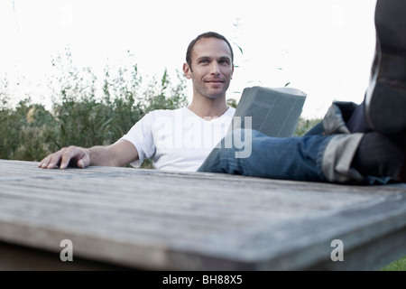 A man sitting at an outdoor table reading a magazine, non-urban scene Stock Photo