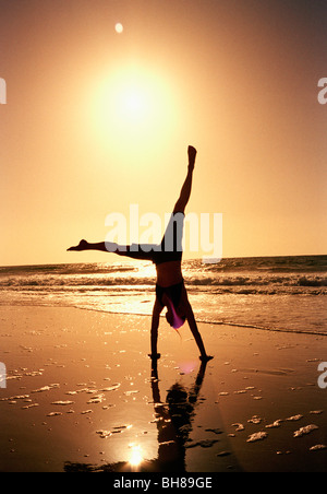 A woman doing a cartwheel on a beach at sunset Stock Photo