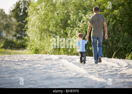 Rear view of a man and a young boy walking hand in hand Stock Photo