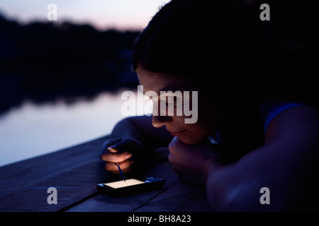A woman using an electronic organizer while lying on a jetty, dusk Stock Photo