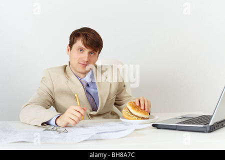 Young businessman is going to eat a delicious sandwich without interrupting work Stock Photo