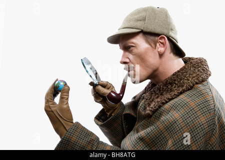 A man dressed up as Sherlock Holmes looking at a tiny globe through a magnifying glass Stock Photo