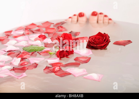 Toes poking out of bath water with rose petals and roses floating in it