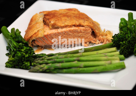 Salmon en croute with broccoli and asparagus on white serving plate on black background Stock Photo