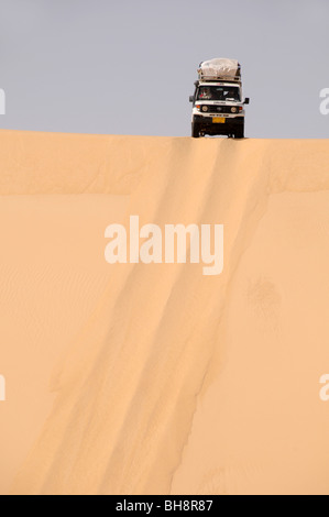 A desert safari land cruiser 4x4 jeep crests a giant sand dune in the Great Sand Sea of the Western Desert, Egyptian Sahara, Egypt. Stock Photo