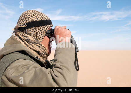 A Saharan guide looks through his binoculars towards the sand dunes in the Gilf Kebir region of the Western Desert, in southwest Egypt. Stock Photo
