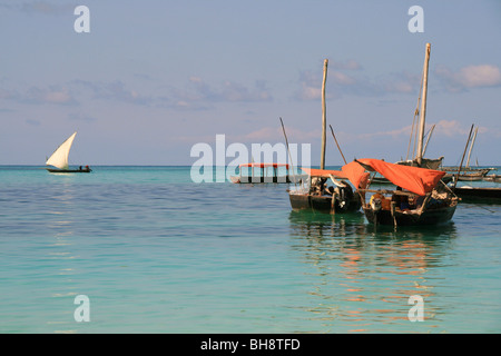 Fishermen shelter from the sun under red canvas onboard their wooden fishing boats off nungwi beach, zanzibar. Stock Photo