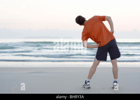 Runner doing stretching exercises on a beach early in the morning Stock Photo