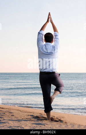 Businessman doing yoga on the beach Stock Photo