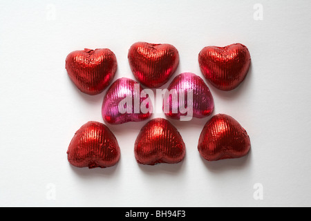 six red and two pink heart shaped caramel chocolates arranged on a white background  - ideal for Valentine day, Valentines day Stock Photo