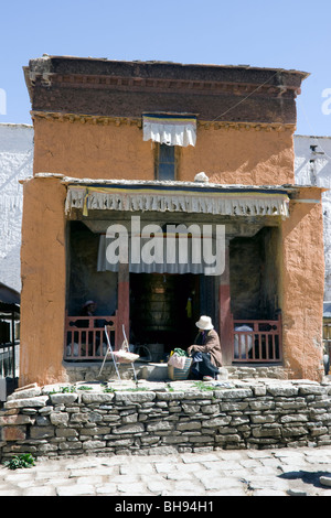 old tibetan woman outside temple with prayer wheel in the old town area of gyantse Stock Photo