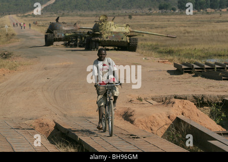 Angolan boy on bicycle rides past two Cuban tanks which were abandoned at Longa  in Southern Angola, Africa. Stock Photo