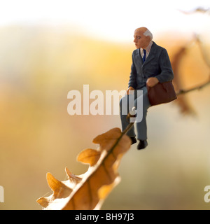 Old man / senior figurine sitting on a branch of tree in autumn - retirement, freedom, environment, loss, loneliness concept Stock Photo