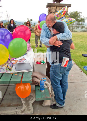 The father of a young adult suicide is hugged by well-wishers at an outdoor memorial service in Laguna Beach, California. Stock Photo