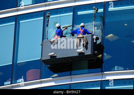 Window cleaners suspended in a cradle washing glass curtain walls of large office building with a glass facade, London Stock Photo