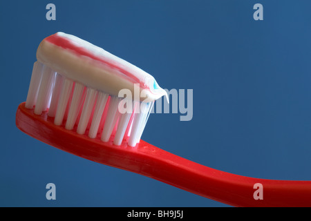 close up of striped toothpaste on red toothbrush set against blue background Stock Photo
