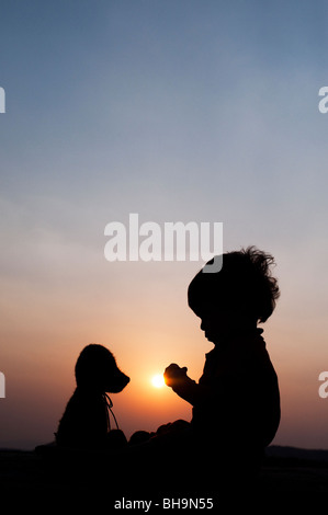Little boy sitting opposite his teddy bear at sunset. Silhouette. India Stock Photo