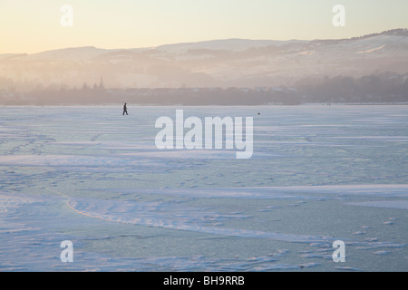 Man walking on a frozen Castle Semple Loch in winter, Clyde Muirshiel Regional Park, Lochwinnoch, Renfrewshire, Scotland, UK