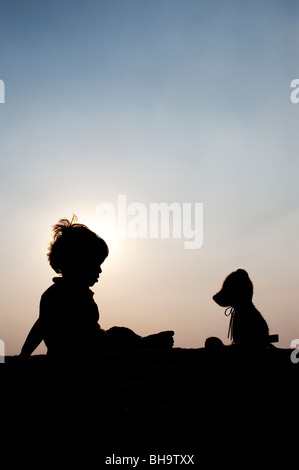 Little boy sitting opposite his teddy bear at sunset. Silhouette. India Stock Photo