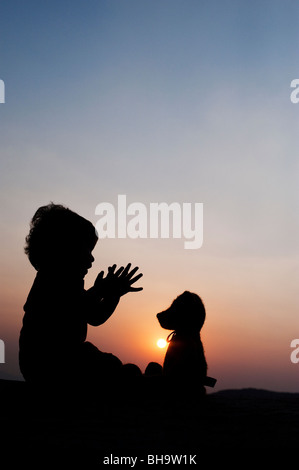 Little boy clapping his hands with a teddy bear at sunset. Silhouette. India Stock Photo