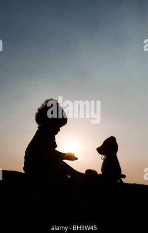 Little boy holding the sun with a teddy bear at sunset. Silhouette. India Stock Photo