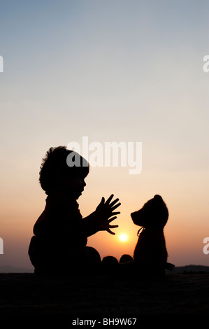 Little boy clapping his hands with a teddy bear at sunset. Silhouette. India Stock Photo