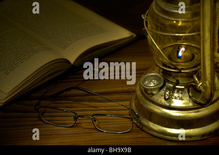 Cosy reading. Old book and glasses with vintage tilly lamp on a wooden desk. Retro style. Stock Photo