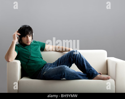 Good-looking young man seated on the couch listen music Stock Photo