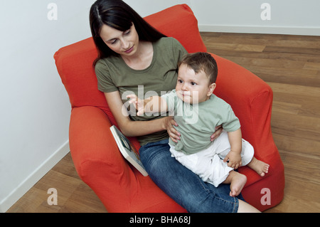 Young woman and baby boy sitting on arm chair with a book