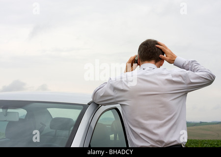 Worried businessman talking on cell phone beside his car Stock Photo