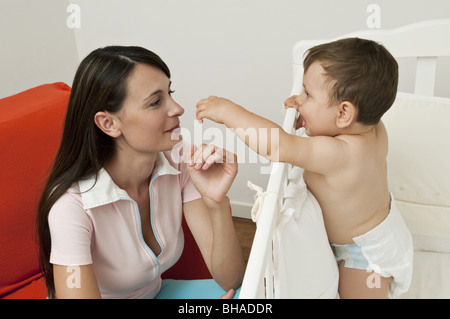 Young woman on arm chair and baby boy in crib Stock Photo