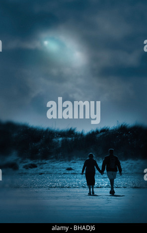 middle aged man and woman walking hand in hand towards grassy bank in moonlight Stock Photo