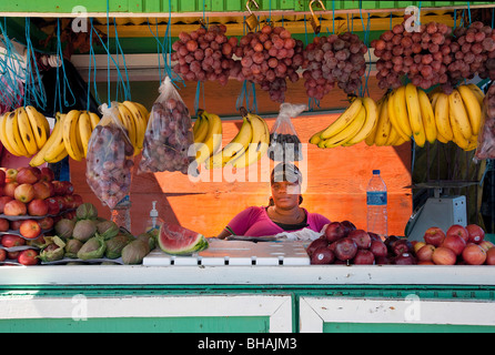 Fruit seller behind counter on market day  with apples and tropical fruit on display Tobago Caribbean Stock Photo