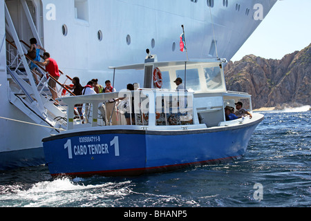 Cruise ship tender boat unloading passengers into side of ship. Walkway to open door. Beach in distant. Ocean water. Stock Photo