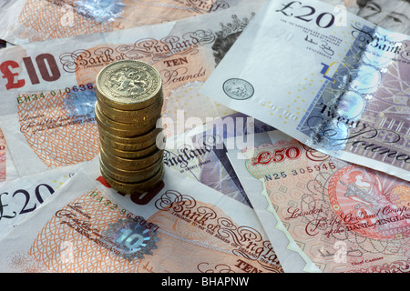 Pile of one pound coins on a background of British bank notes, fifty, twenty and ten pound notes, in close up. Stock Photo