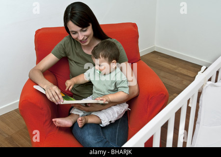 Young woman and baby boy sitting on arm chair reading a book