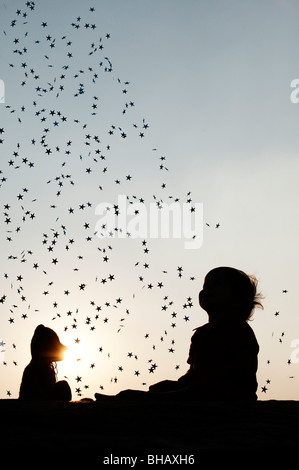 Little boy with his teddy bear watching falling stars at sunset. Silhouette. India Stock Photo