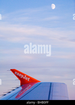 Easyjet flight Airbus A319 plane / aircraft wing, blue sky, & moon, while flying across Europe. Wingtip on Airbus airliner is called sharklet sharklets. Stock Photo