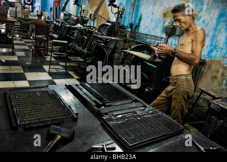 A Cuban master printer, leant against a printing machine, waiting for a new load in the print shop, Santiago de Cuba, Cuba. Stock Photo