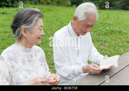 Japan, Tokyo Prefecture, Senior couple in park, man reading book and woman knitting Stock Photo