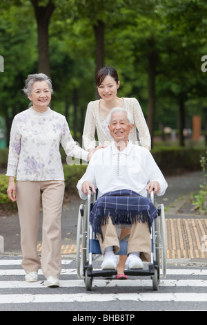 Japan, Tokyo Prefecture, Woman pushing senior man in wheelchair, crossing road Stock Photo