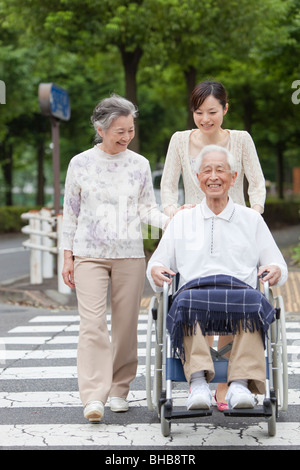 Japan, Tokyo Prefecture, Woman pushing senior man in wheelchair, crossing road Stock Photo