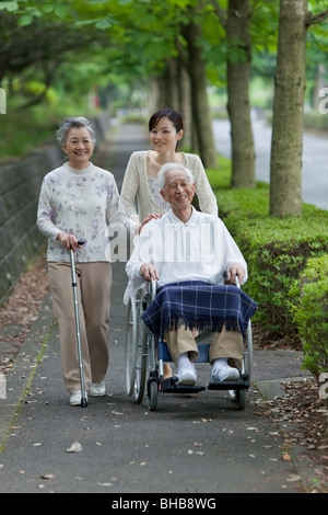 Japan, Tokyo Prefecture, Woman pushing senior man in wheelchair through footpath, smiling Stock Photo