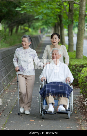 Japan, Tokyo Prefecture, Woman pushing senior man in wheelchair through footpath, smiling Stock Photo