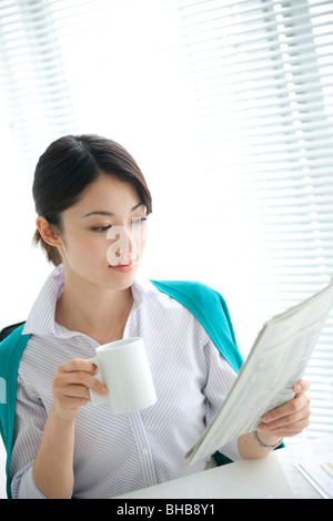 Japan, Osaka Prefecture, Businesswoman with coffee cup reading newspaper Stock Photo