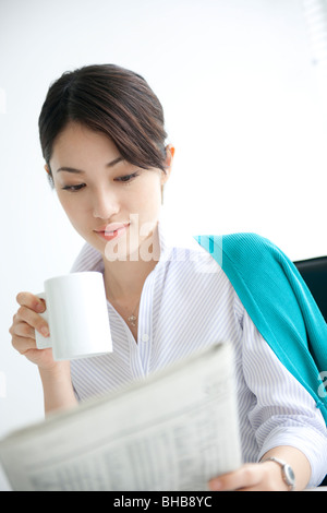 Japan, Osaka Prefecture, Businesswoman with coffee cup reading newspaper Stock Photo