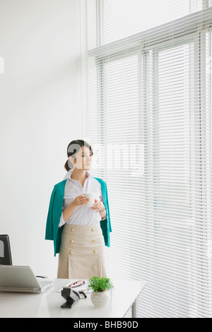 Japan, Osaka Prefecture, Businesswoman with coffee cup, looking away Stock Photo