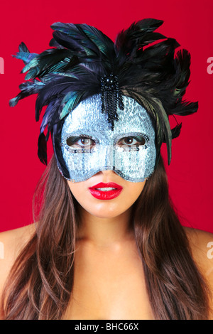 Beautiful brunette woman wearing a masqurade mask against a bright red background. Stock Photo