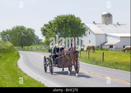 Amish horse and carriage driving past barn in Lancaster County, Pennsylvania Stock Photo